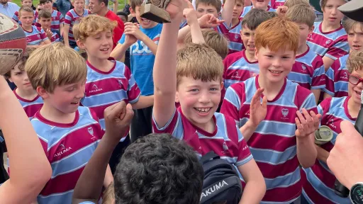 A group of young boys in striped jerseys celebrates, with one boy joyfully holding a trophy.