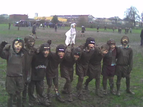 A group of muddy children smiling and posing playfully on a wet field.